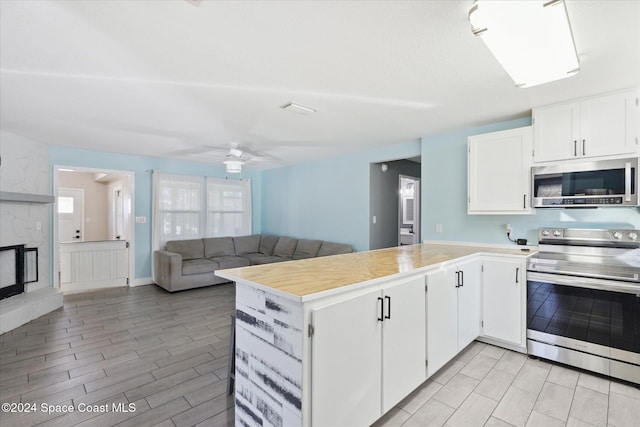 kitchen with white cabinets, light hardwood / wood-style flooring, ceiling fan, kitchen peninsula, and stainless steel appliances