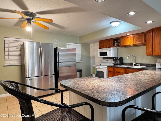 kitchen with a kitchen bar, a textured ceiling, white appliances, sink, and light tile patterned flooring