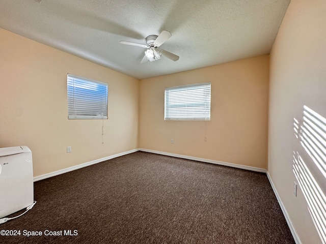 empty room featuring ceiling fan, dark carpet, and a textured ceiling