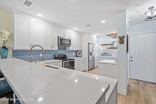 kitchen featuring white cabinets, decorative backsplash, light wood-type flooring, appliances with stainless steel finishes, and kitchen peninsula