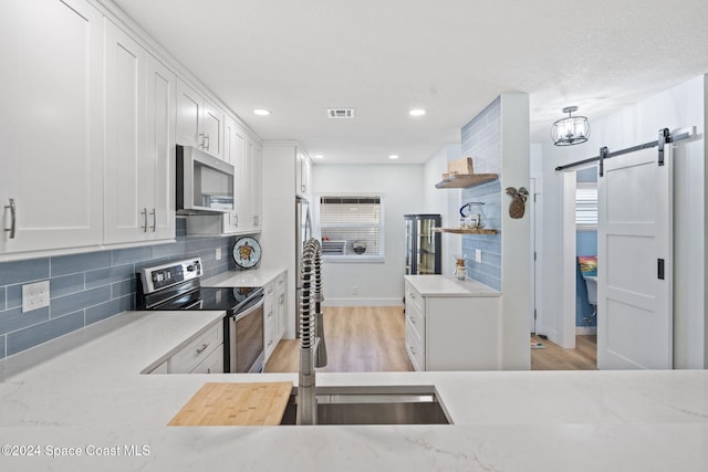 kitchen with white cabinets, appliances with stainless steel finishes, a barn door, and light hardwood / wood-style flooring