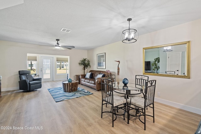 dining space featuring ceiling fan with notable chandelier, light wood-type flooring, and a textured ceiling