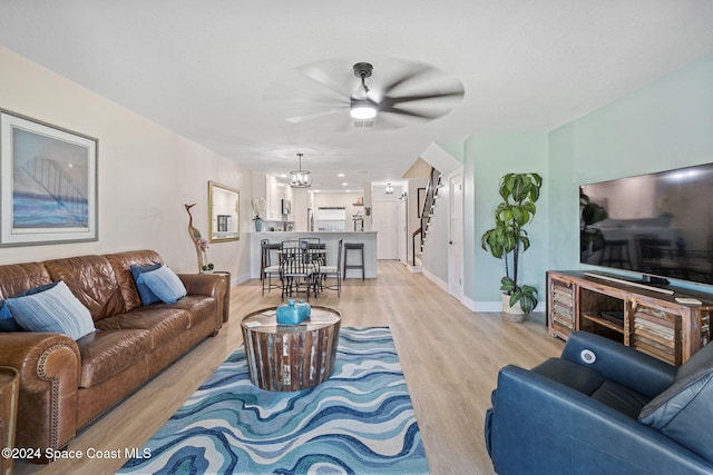 living room featuring ceiling fan with notable chandelier and light wood-type flooring