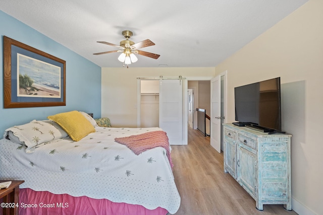 bedroom featuring a walk in closet, light hardwood / wood-style flooring, ceiling fan, a barn door, and a closet