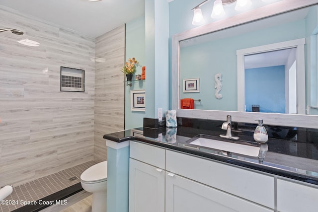 bathroom with hardwood / wood-style floors, vanity, toilet, and tiled shower