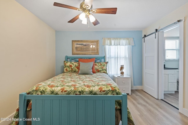 bedroom with a barn door, ceiling fan, and light wood-type flooring