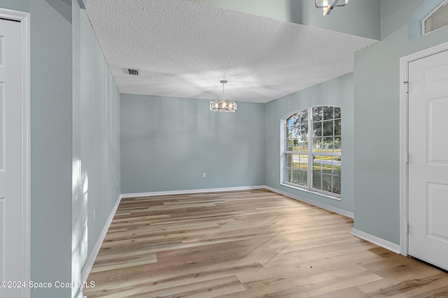 unfurnished dining area featuring a chandelier, a textured ceiling, and light wood-type flooring