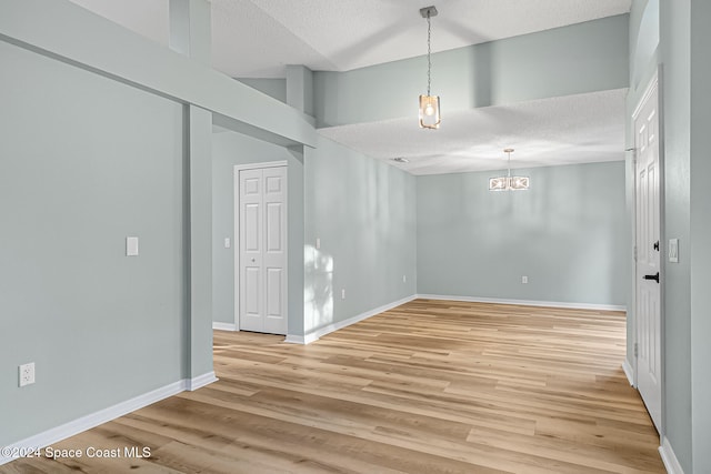 unfurnished room with a chandelier, a textured ceiling, and light wood-type flooring