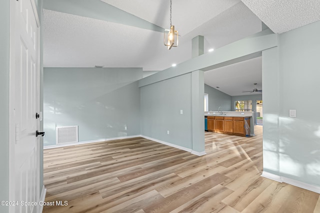 unfurnished living room featuring light wood-type flooring, a textured ceiling, ceiling fan, sink, and lofted ceiling