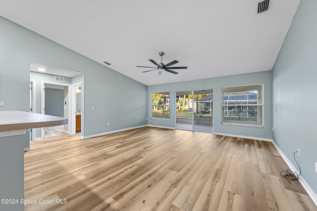 unfurnished living room featuring a textured ceiling, light hardwood / wood-style floors, vaulted ceiling, and ceiling fan