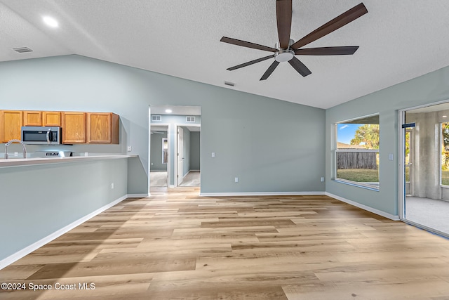 unfurnished living room with a textured ceiling, light hardwood / wood-style flooring, vaulted ceiling, and ceiling fan