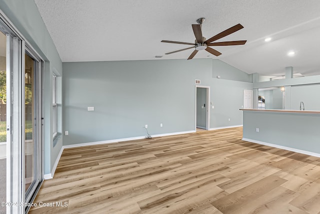 unfurnished living room featuring ceiling fan, sink, light hardwood / wood-style floors, a textured ceiling, and lofted ceiling