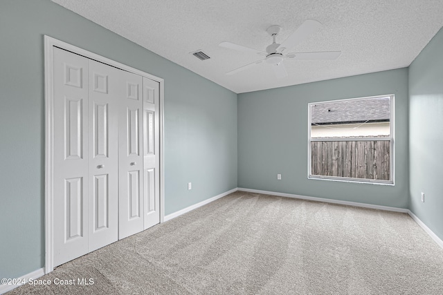 unfurnished bedroom featuring a textured ceiling, carpet floors, a closet, and ceiling fan