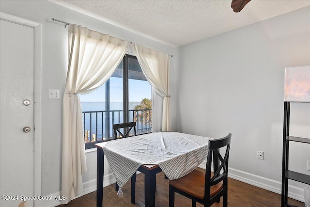 dining area featuring a water view, dark wood-type flooring, and a textured ceiling