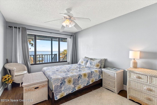 bedroom with ceiling fan, a water view, a textured ceiling, and dark hardwood / wood-style flooring