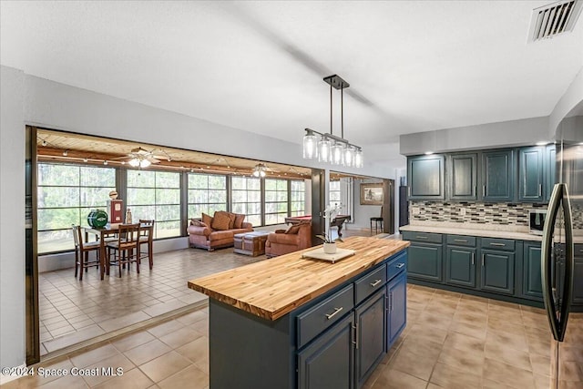 kitchen with backsplash, ceiling fan, decorative light fixtures, a kitchen island, and butcher block counters