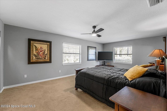 bedroom with a textured ceiling, light colored carpet, and ceiling fan