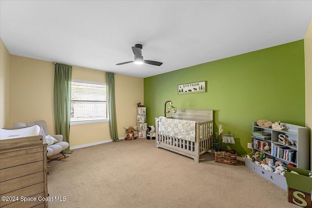 carpeted bedroom with a crib and ceiling fan