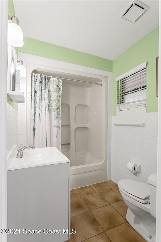 full bathroom with shower / bathtub combination with curtain, tile patterned floors, toilet, vanity, and tile walls