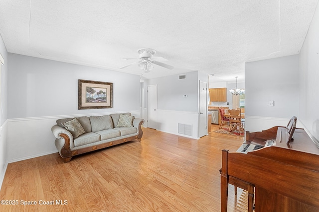 living room with ceiling fan with notable chandelier, a textured ceiling, and light hardwood / wood-style flooring