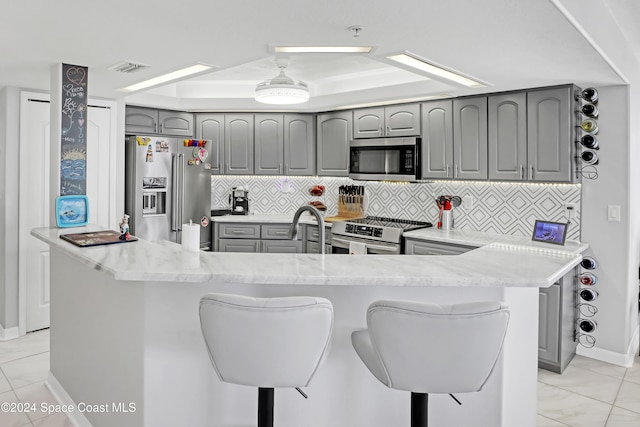 kitchen with gray cabinetry, premium appliances, backsplash, and a breakfast bar area