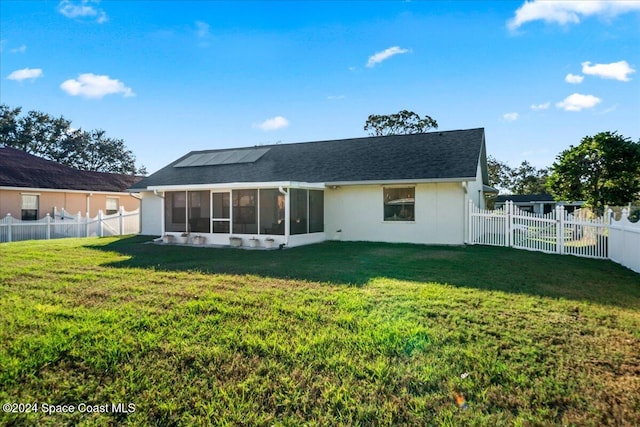 rear view of property with a lawn, a sunroom, and solar panels