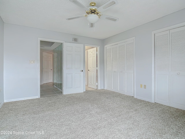 unfurnished bedroom featuring a textured ceiling, ceiling fan, light carpet, and multiple closets