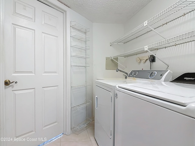 clothes washing area with washer and dryer, light tile patterned floors, and a textured ceiling