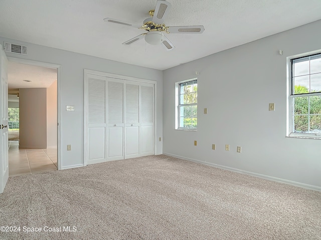 unfurnished bedroom with light carpet, a textured ceiling, a closet, and ceiling fan