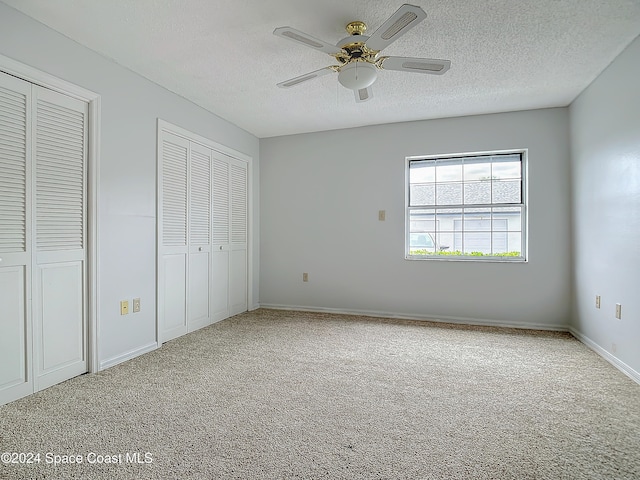 unfurnished bedroom featuring a textured ceiling, ceiling fan, carpet floors, and two closets