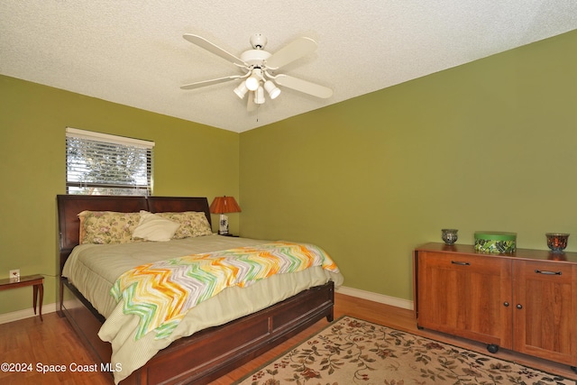 bedroom with ceiling fan, wood-type flooring, and a textured ceiling