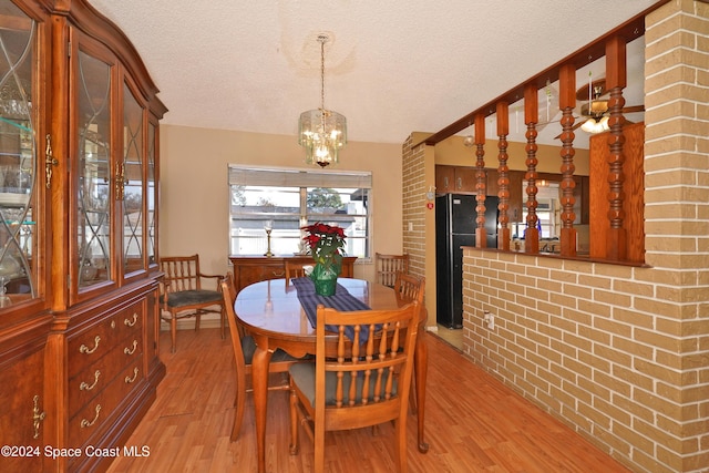 dining area with a notable chandelier, a textured ceiling, brick wall, and light hardwood / wood-style flooring