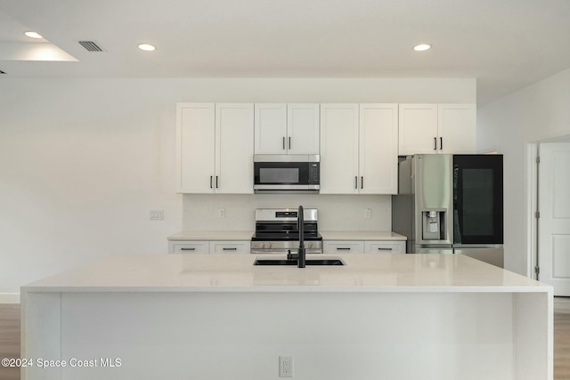 kitchen featuring white cabinets, light hardwood / wood-style floors, stainless steel appliances, and an island with sink