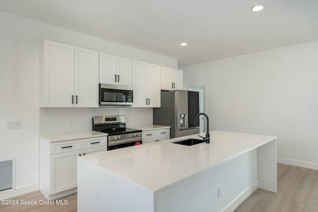 kitchen featuring white cabinets, sink, appliances with stainless steel finishes, and an island with sink