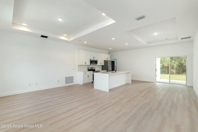 kitchen with a raised ceiling, a center island with sink, white cabinets, and stainless steel appliances