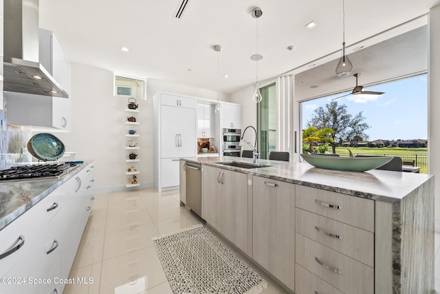 kitchen with wall chimney range hood, sink, appliances with stainless steel finishes, decorative light fixtures, and light tile patterned flooring