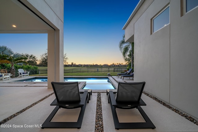 patio terrace at dusk featuring a fenced in pool