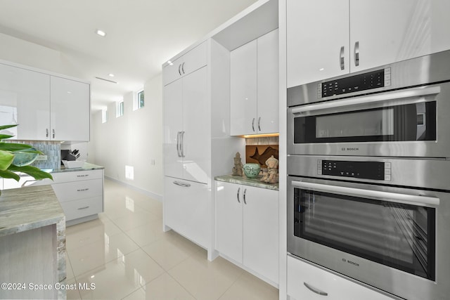 kitchen with light stone countertops, white cabinetry, light tile patterned floors, and stainless steel double oven