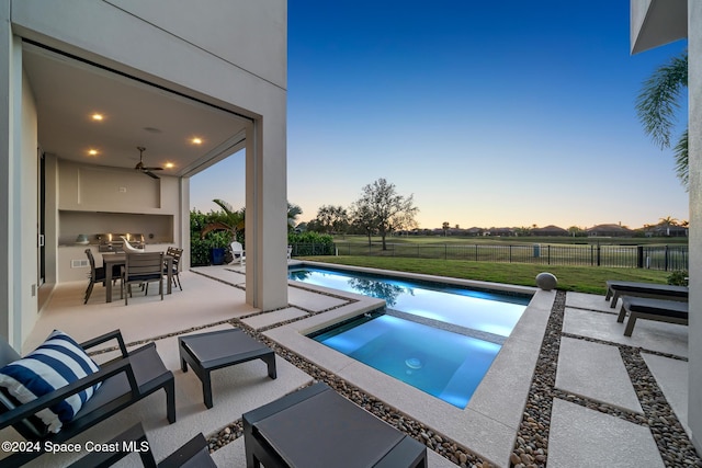 pool at dusk with ceiling fan, an in ground hot tub, and a patio