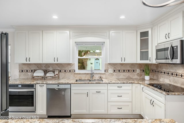 kitchen with light stone counters, stainless steel appliances, white cabinetry, and sink