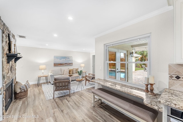 living room featuring crown molding, french doors, a fireplace, and light hardwood / wood-style flooring