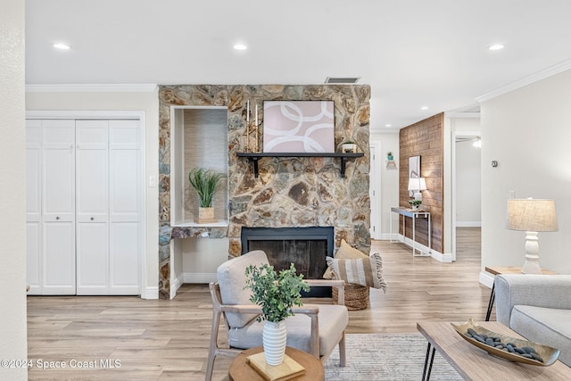 living room with light hardwood / wood-style floors, a stone fireplace, and crown molding