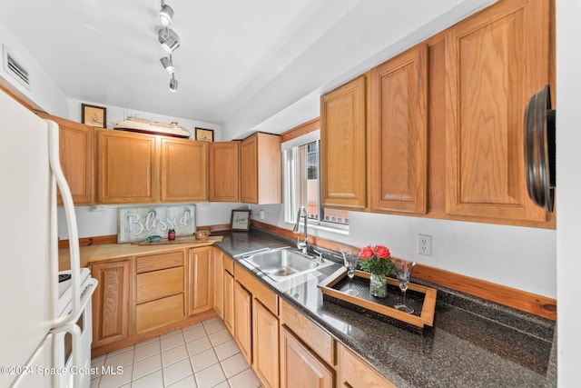 kitchen featuring white appliances, rail lighting, sink, dark stone countertops, and light tile patterned floors