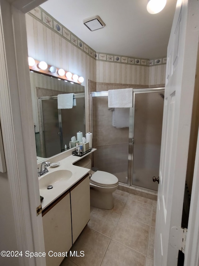 bathroom featuring toilet, vanity, tile patterned floors, and a shower with door