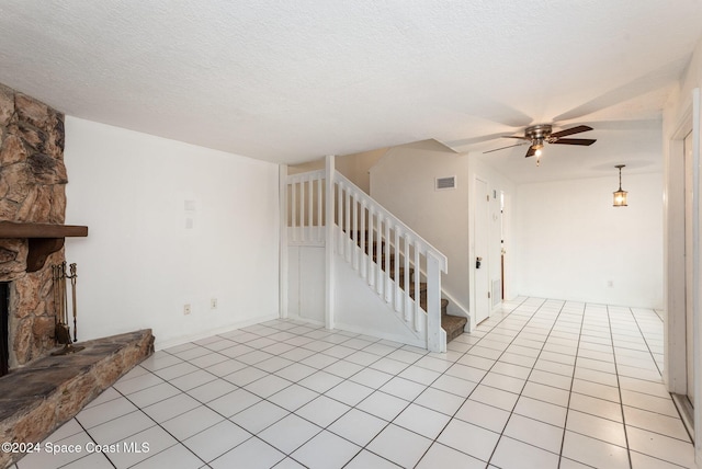 unfurnished living room featuring a stone fireplace, ceiling fan, light tile patterned floors, and a textured ceiling