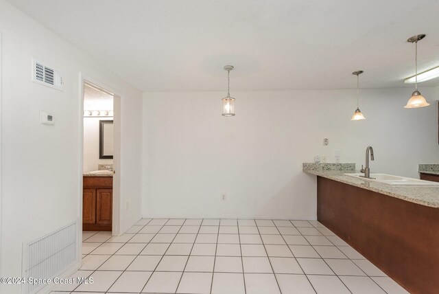 interior space featuring light tile patterned flooring, light stone counters, hanging light fixtures, and sink