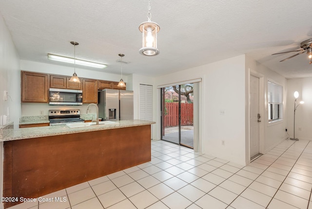 kitchen with kitchen peninsula, light stone counters, stainless steel appliances, sink, and decorative light fixtures