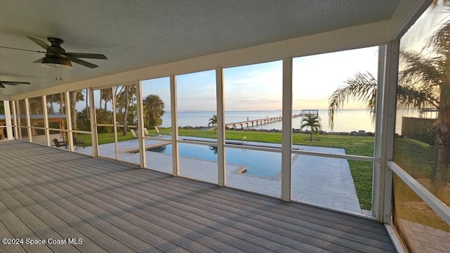 unfurnished sunroom with ceiling fan, a water view, and a wealth of natural light