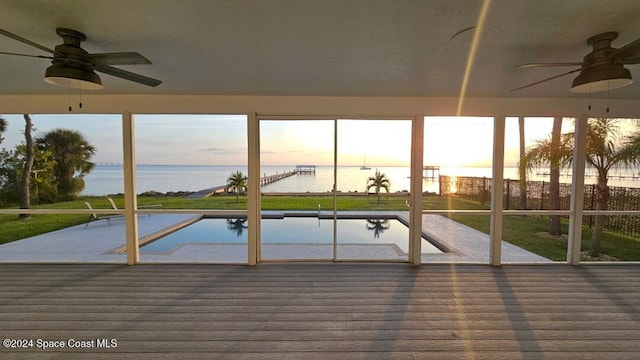 unfurnished sunroom featuring ceiling fan and a water view