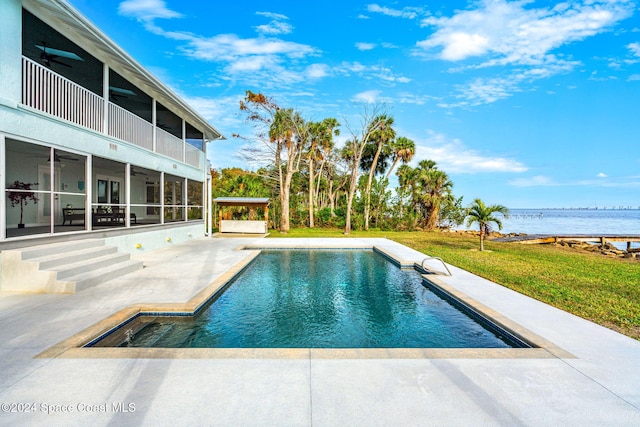 view of swimming pool featuring a sunroom, a water view, a patio, ceiling fan, and a lawn